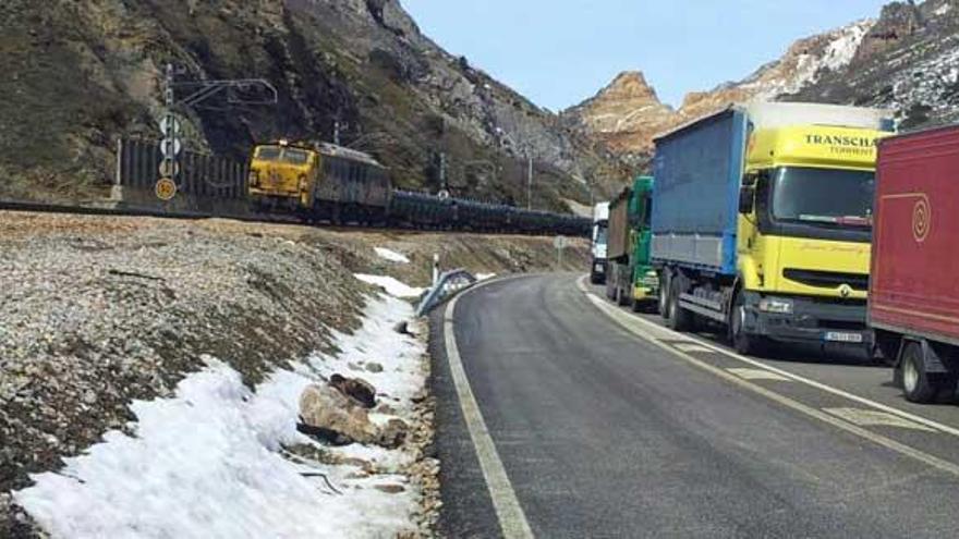 Un tren de mercancías y varios vehículos parados por el corte tanto en la vía férrea como en la carretera en Ciñera.