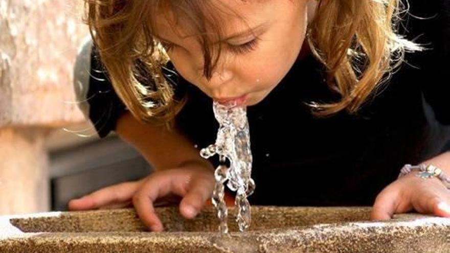 Una niña bebe agua en una fuente pública en Alicante.