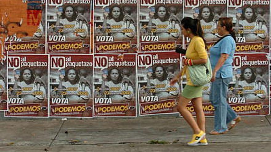 Dos mujeres pasan frente a un muro con propaganda de los partidos de oposición, en Caracas (Venezuela).
