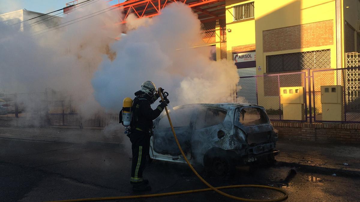 Los bomberos apagan el coche incendiado.