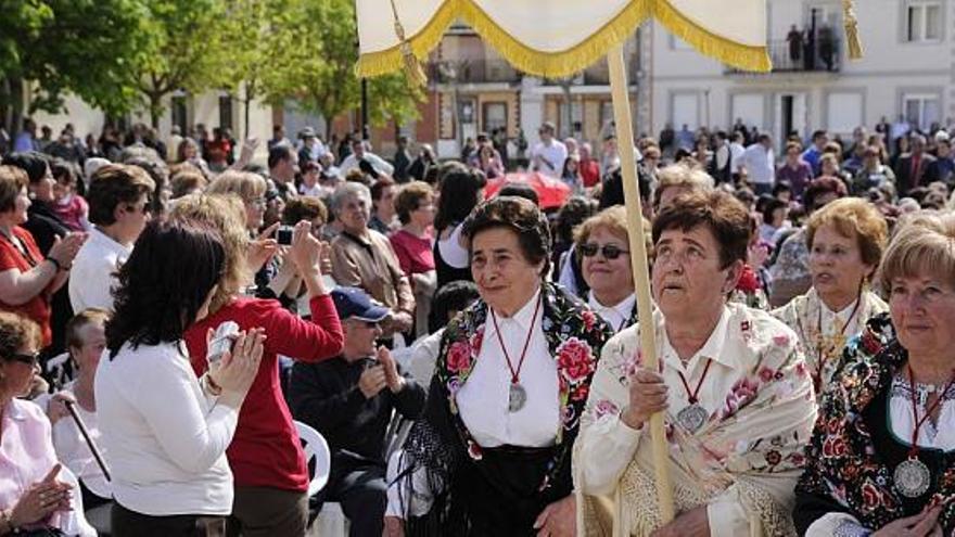 En primer plano, varias mujeres ataviadas con indumentaria tradicional y portando estandartes de sus respectivos pueblos en la Plaza Mayor.