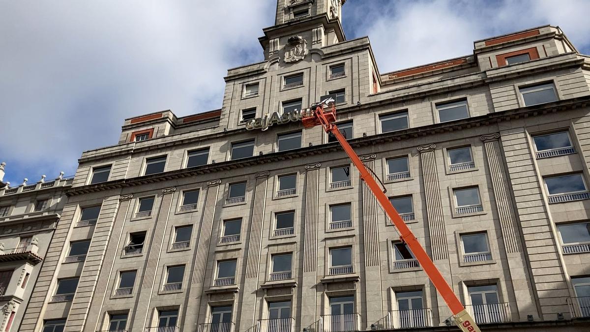 Despliegan una grúa en La Escandalera para medir el cartel de la oficina principal de Liberbank ante un inminente cambio de cartel