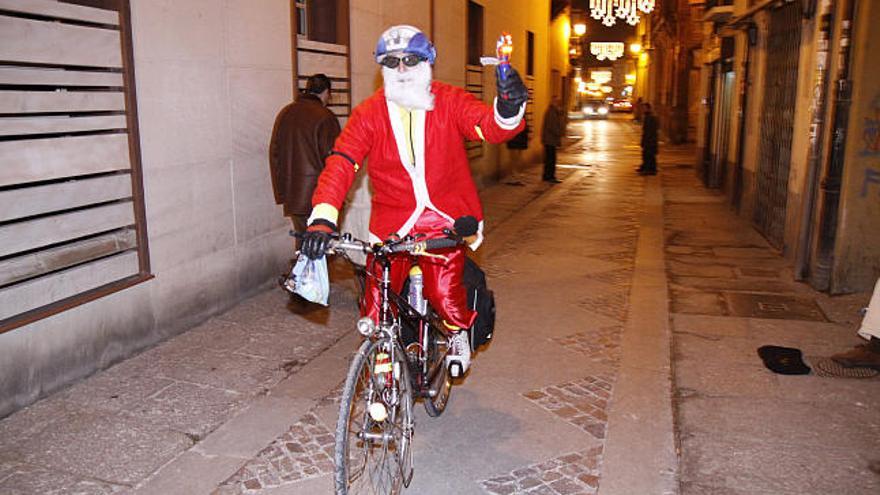 Un Papá Noel en bicicleta recorre las calles ya iluminadas con las luces de Navidad.