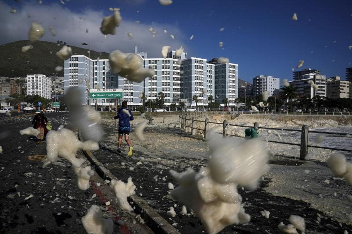 Un hombre corre a través de la espuma del mar, mientras un frente frío estacional se movía sobre la Península del Cabo, después de una semana de clima severo e inundaciones en Ciudad del Cabo, Sudáfrica, el 19 de junio de 2023.