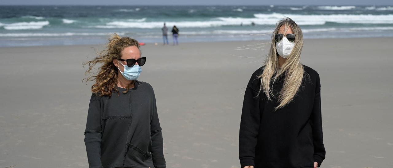 Dos mujeres con mascarilla en la playa.