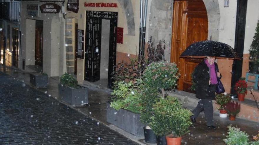 Una mujer camina ayer por las calles de Morella mientras caen unos copos de nieve.