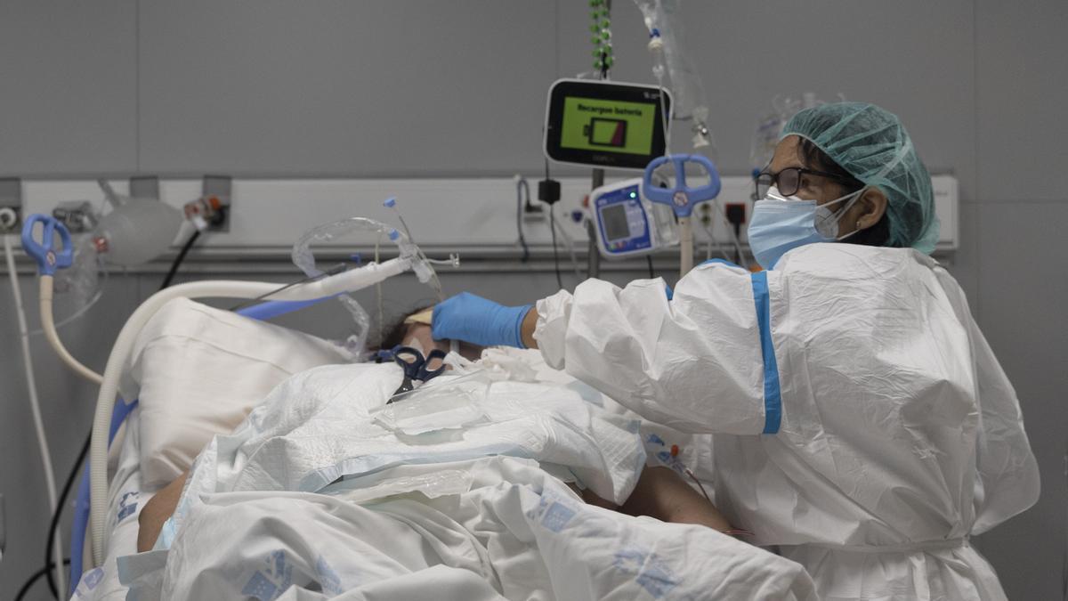 Un sanitario junto a un paciente ingresado en la UCI del Hospital Isabel Zendal de Madrid.