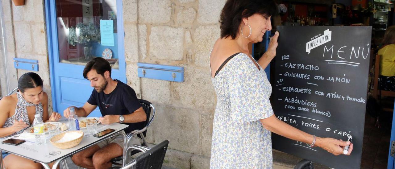 Gente comiendo en una terraza mientras su propietaria sujeta un cartel con el menú del día.  / MARTA G. BREA