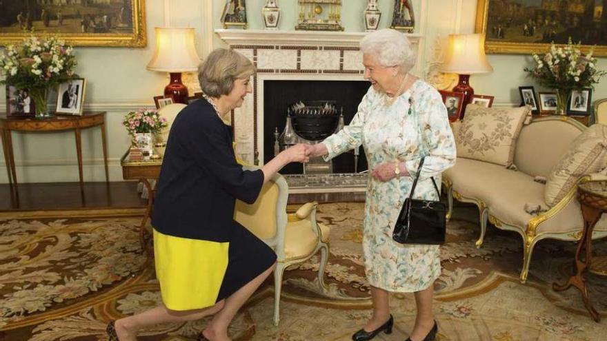 Theresa May se arrodilla ante la reina Isabel II. // Efe