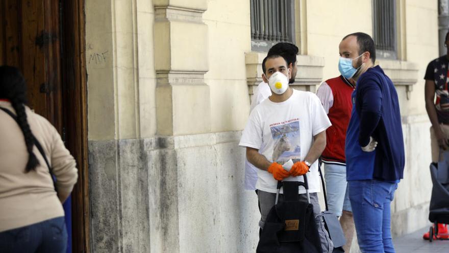 Varias personas esperan su turno para recibir comida.