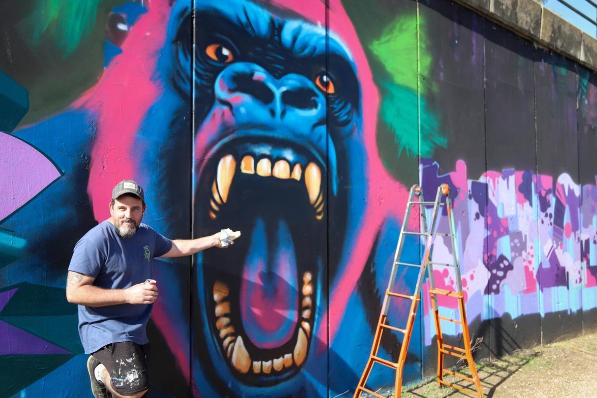 El grafittero montija El Ale bromea simulando dar su bocadillo al orangután que ha pintado.