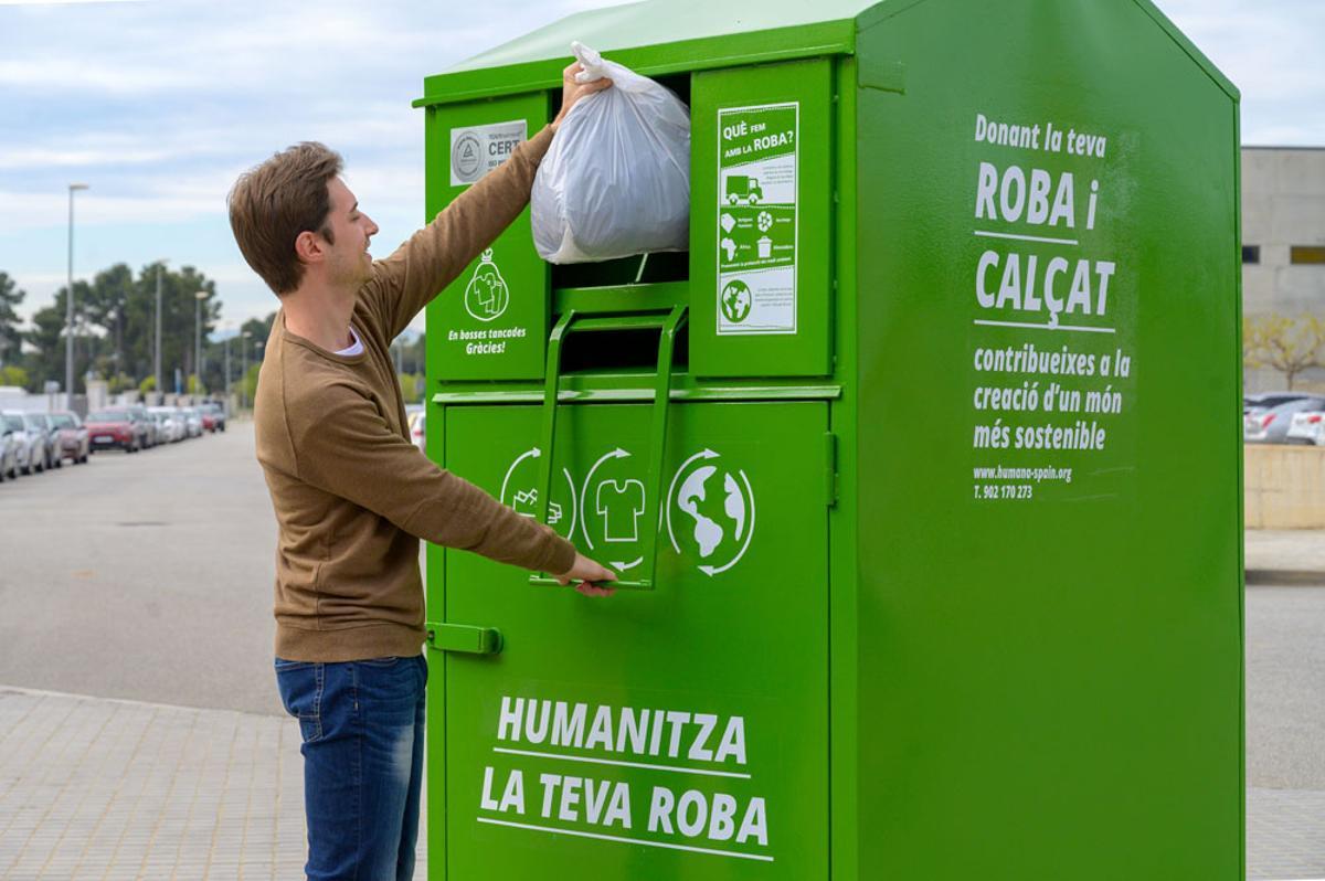 Un joven deposita una bolsa de ropa usada en uno de los 1.500 contenedores verdes que hay en las calles de Catalunya.