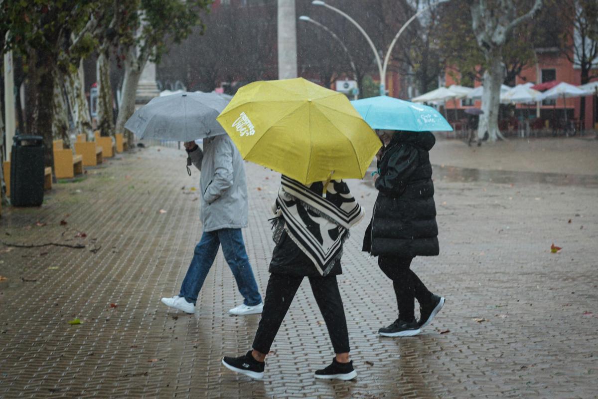 Tres personas se protegen de la lluvia con paraguas en La Alameda.