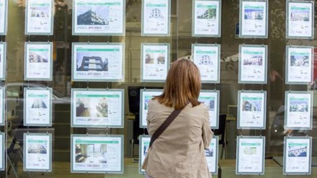 Una viandante observa anuncios de pisos en una inmobiliaria de Barcelona.