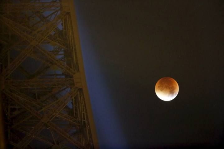 The Moon, appearing next to the Eiffel Tower in a dim red colour, is covered by the Earth's shadow during a total lunar eclipse over Paris