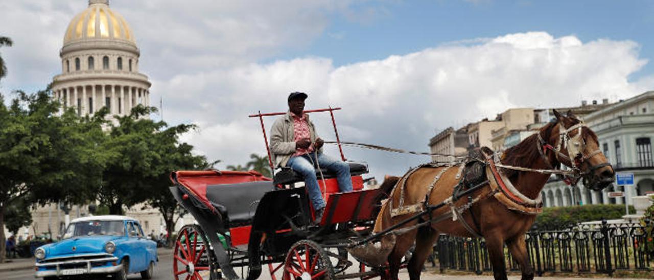 Un coche tirado por caballos y un automóvil clásico circulan por una céntrica calle de La Habana.