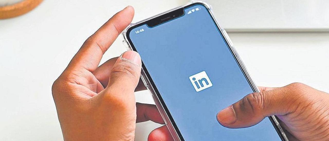 Un hombre abre la aplicación de Linkedin en un móvil.