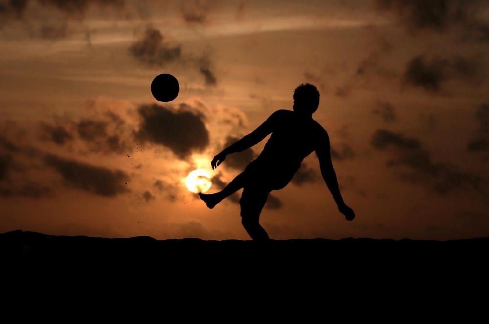 A boy is silhouetted against the sunset as he ...