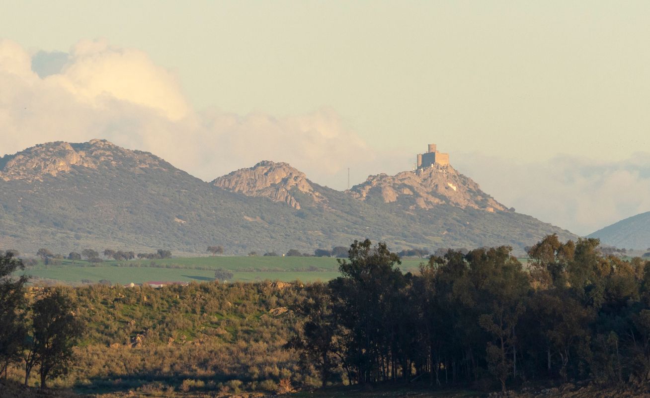 Paisaje al atardecer con el Castillo de Puebla de Alcocer en lo alto de la montaña.