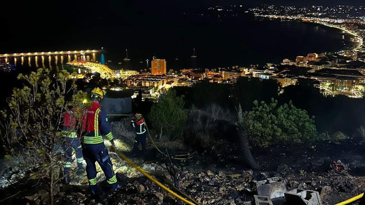 Los bomberos sofocan el terreno calcinado. Abajo, la bahía de Xàbia iluminada.