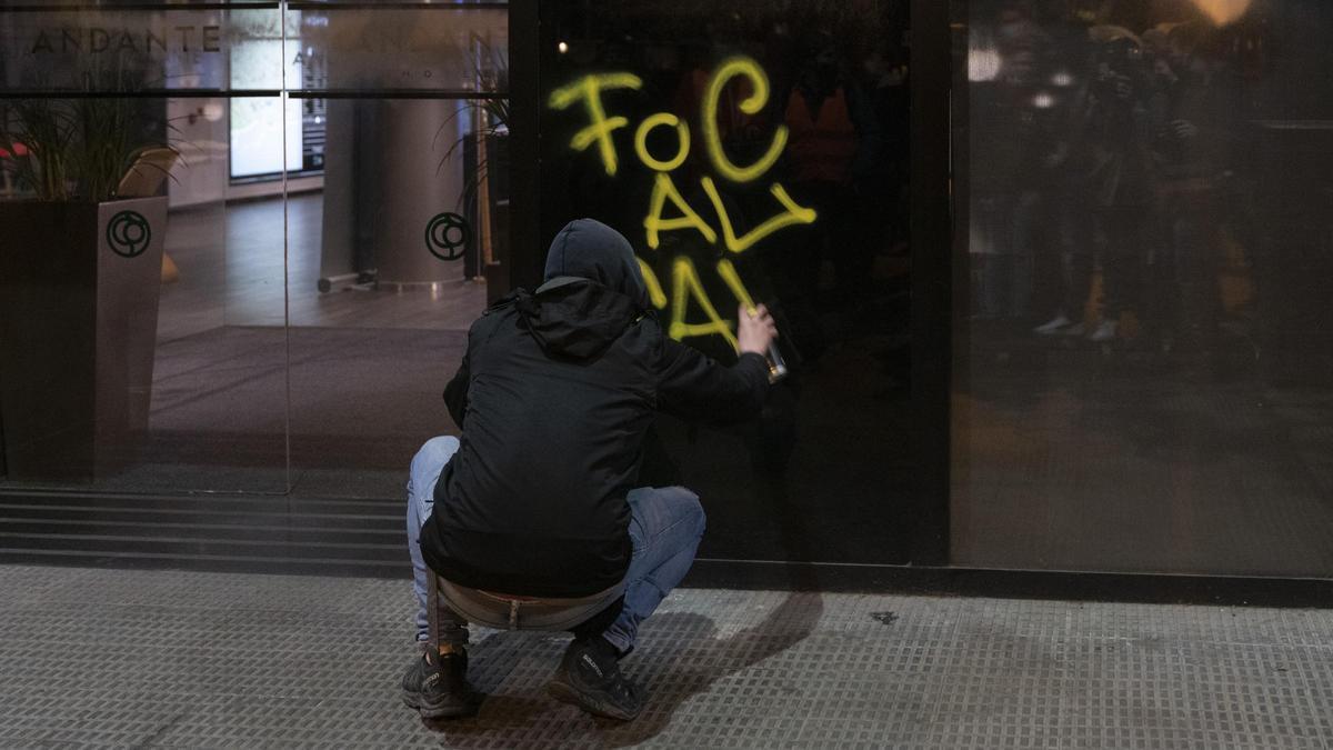 Un encapuchado hace una pintada en los disturbios de Barcelona.