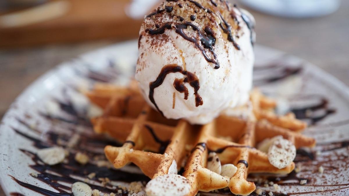 Sugerencia de presentación de un postre que lleva un gofre, una bola de helado, sirope de chocolate, frutos secos y canela