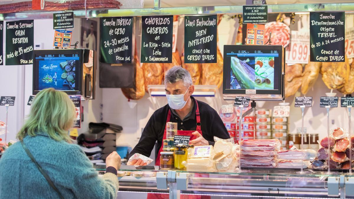 Un charcutero del Mercado Central de Zaragoza atiende a una clienta.