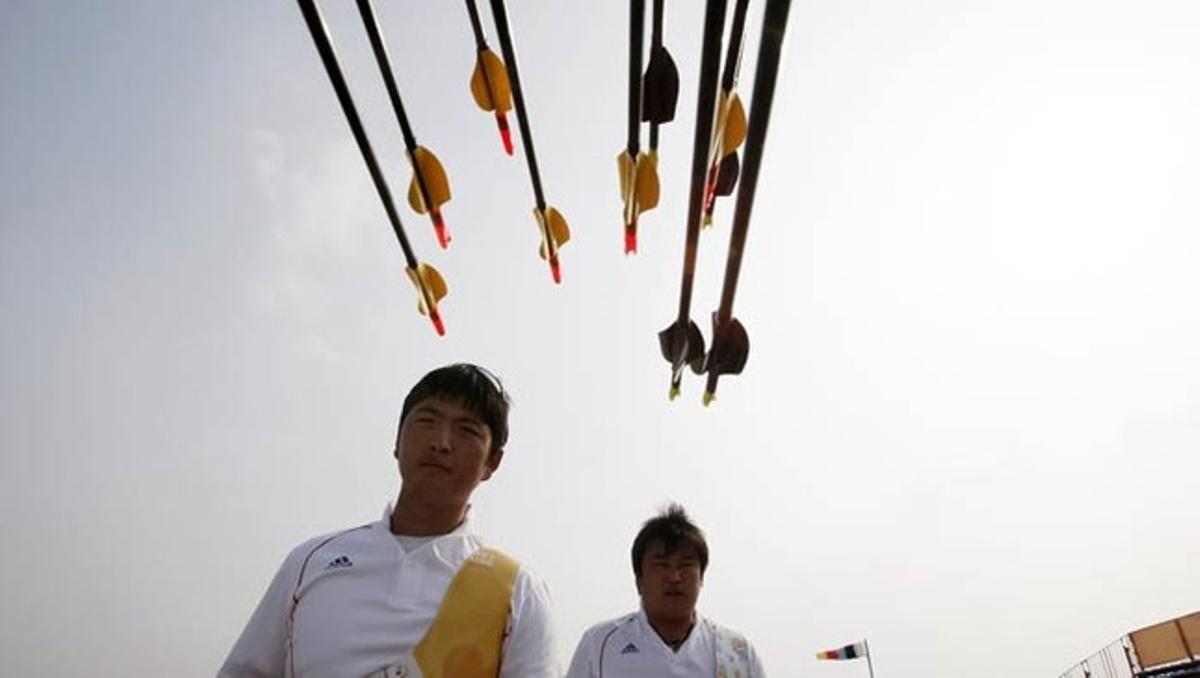 Los surcoreanos Kim Woo-jin y Oh Jin-hyek recogen sus flechas durante las prácticas previas a la competición final de tiro con arco de los Juegos Asiáticos, en Guangzhou (China).