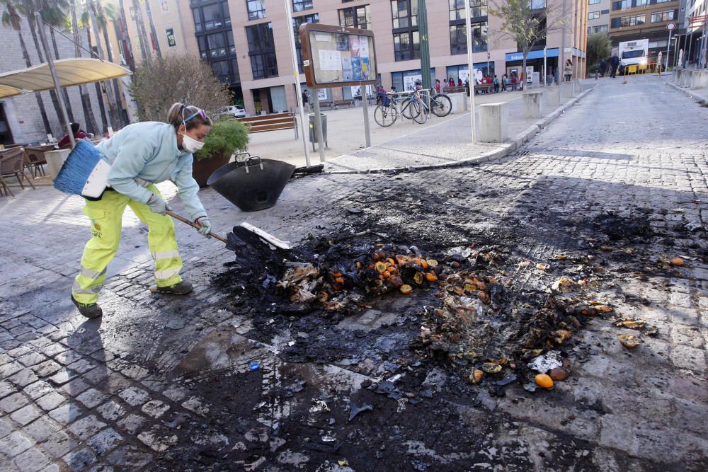 Carrers amb restes de mobiliari urbà cremat, contenidors per terra i treballadors de la brigada treballant