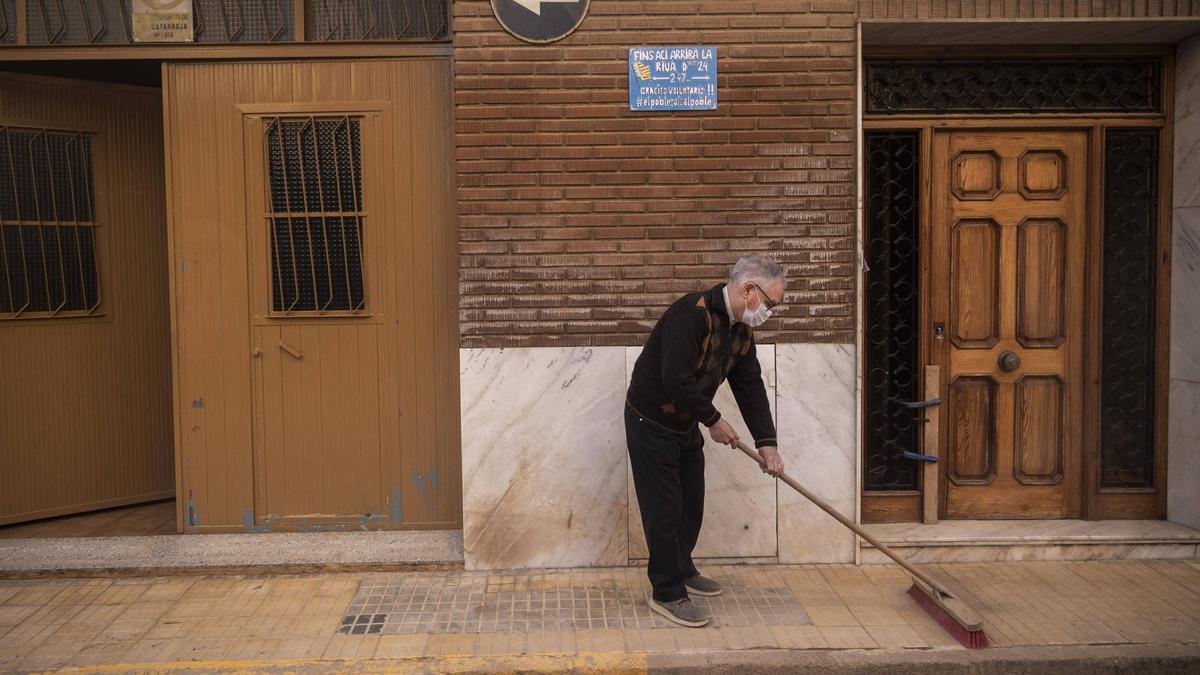Un hombre limpia a la puerta de su casa en Catarroja.