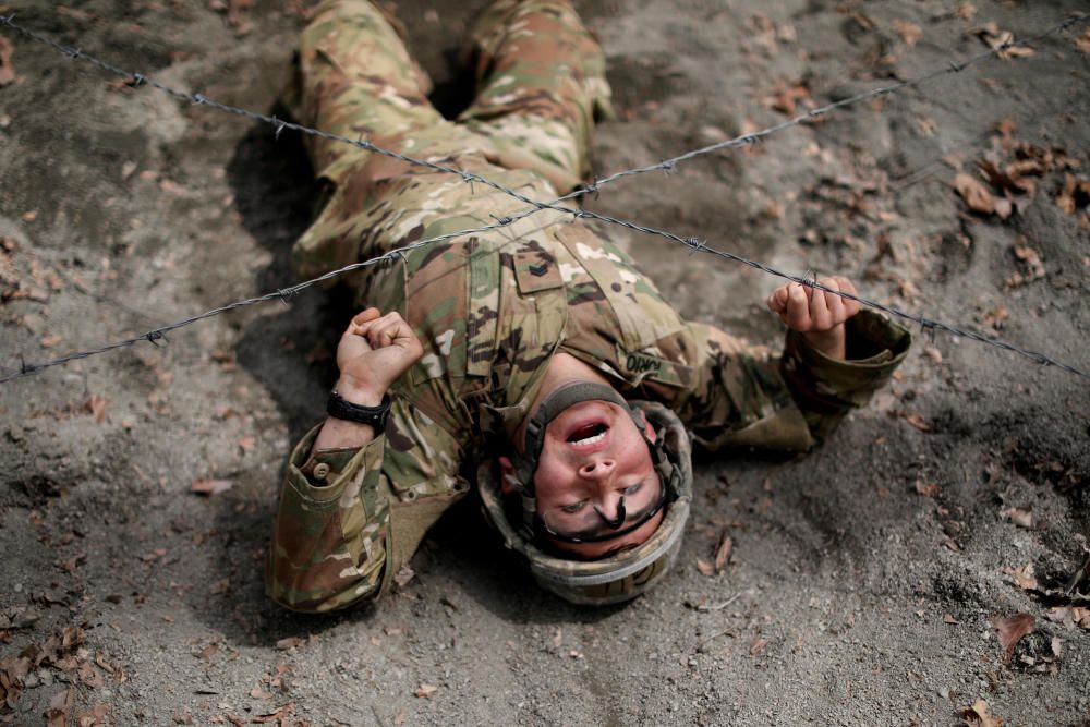 A U.S. Military cadet crawls under a barbed wire ...