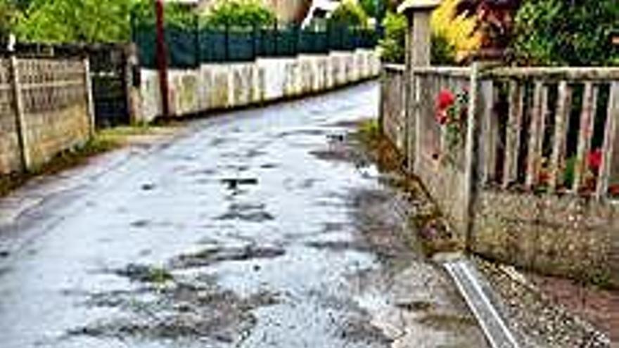 Baches, grietas y desgaste en calles de O Valiño y a la derecha, hasta un poste en medio de la calzada desde hace años.