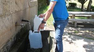 Una persona llena una garrafa con agua de una fuente pública