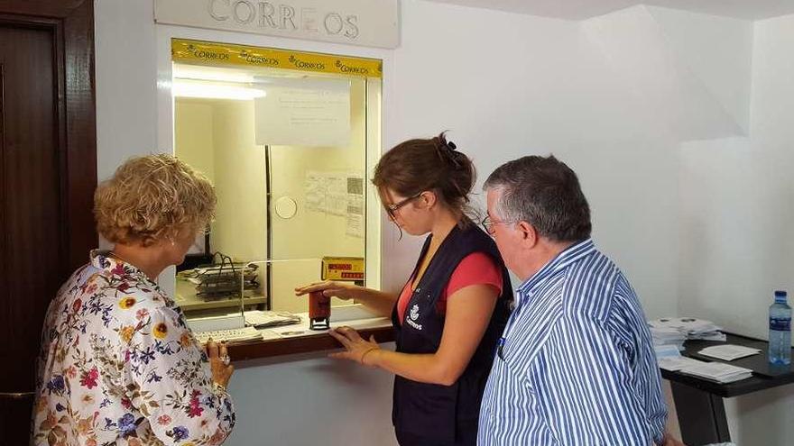 Una operaria de la oficina de Correos en Covadonga (en el centro) muestra el matasellos con la Santina.