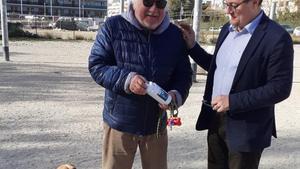 El alcalde de Vilanova, Juan Luis Ruiz, entrega una botella de agua al propietario de un perro, en el marco de la campaña No deixis rastre