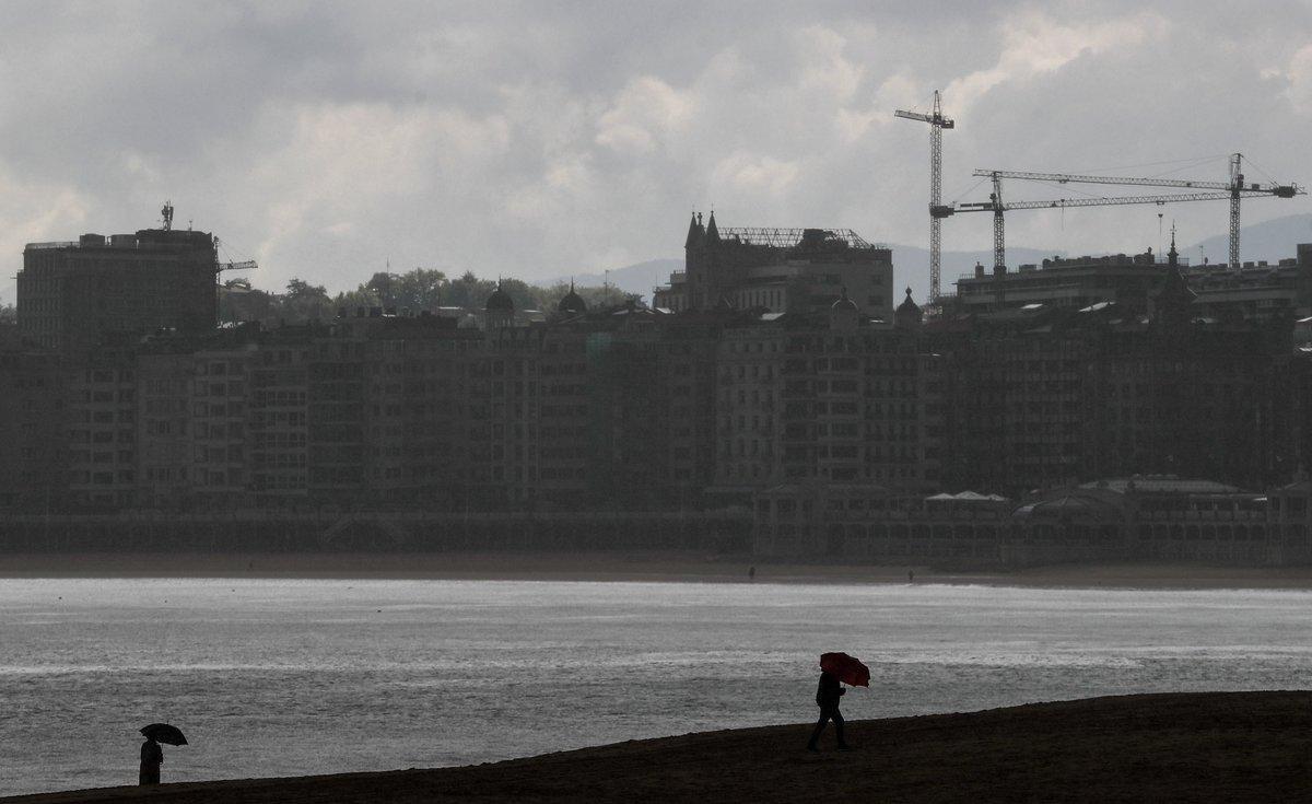 GRAFCAV6407. SAN SEBASTIÁN (ESPAÑA), 09/06/2020.- Unas personas se protegen con paraguas este martes en la playa de Ondarreta en San Sebastián. Los cielos en Euskadi se presentan nubosos o cubiertos con lluvias débiles y chubascos, poco probables en el sur de Álava y más intensas y persistentes en Gipuzkoa y que irán cesando por la tarde, cuando se abrirán claros, temperaturas en ligero ascenso y vientos del noroeste, flojos en general en el interior y más intensos en el litoral. EFE/Juan Herrero