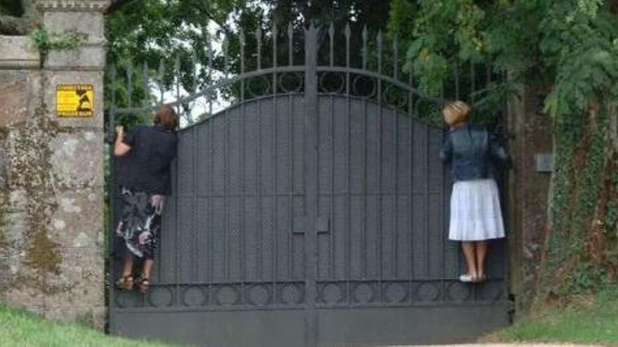 Dos mujeres encaramadas al portalón de entrada del pazo de Meirás.