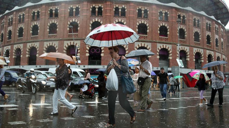 Varias personas cruzando la calle Tarragona en la confluencia con la plaza España de Barcelona bajo la lluvia.