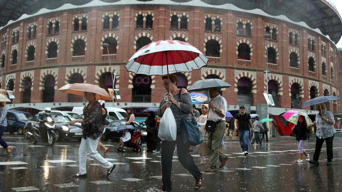 Varias personas cruzando la calle Tarragona en la confluencia con la plaza España de Barcelona bajo la lluvia.