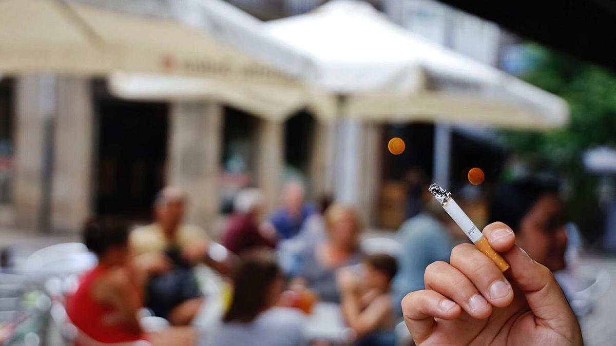 Una persona sostiene un cigarrillo junto a la terraza de un bar. |   // ÓSCAR CORRAL