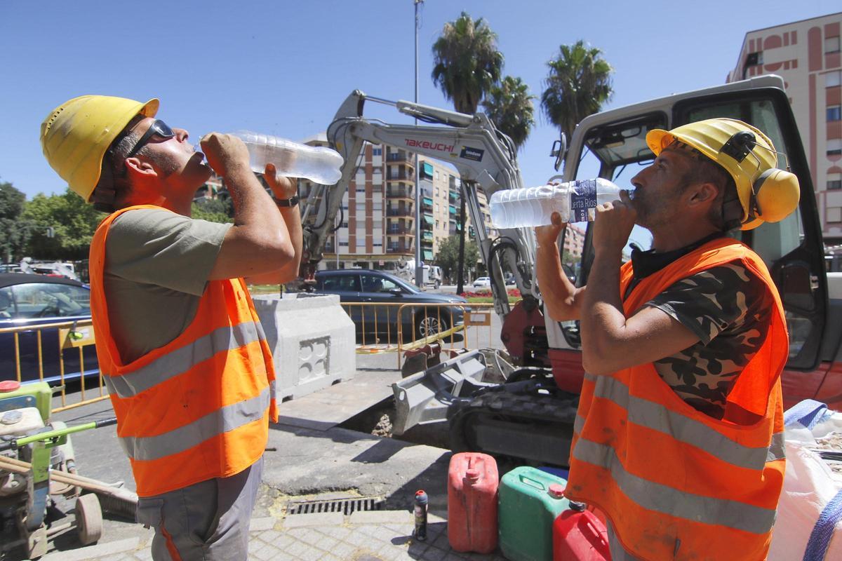 Unos profesionales de la construcción se protegen de las altas temperaturas bebiendo agua.