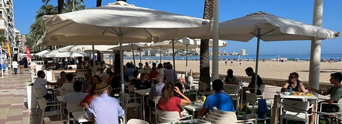 Una terraza del paseo marítimo llena y gente en la playa.