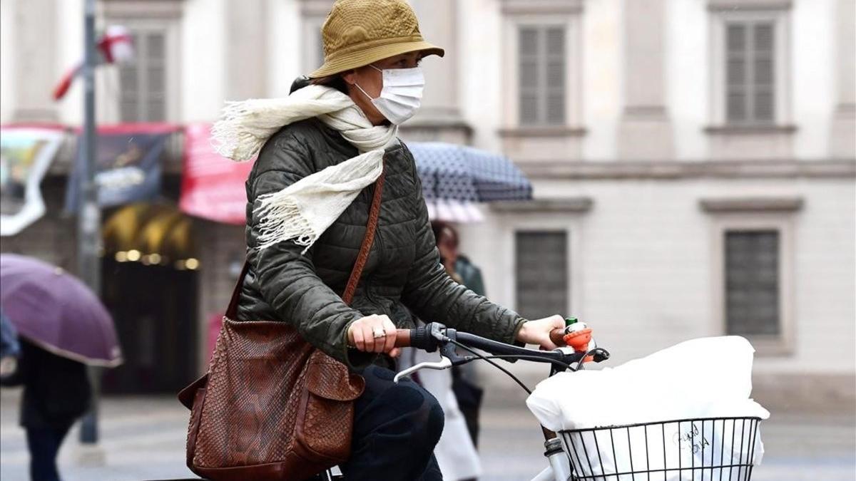 Una mujer con mascarilla para protegerse del coronavirus pedalea por la plaza del Duomo, en Milán