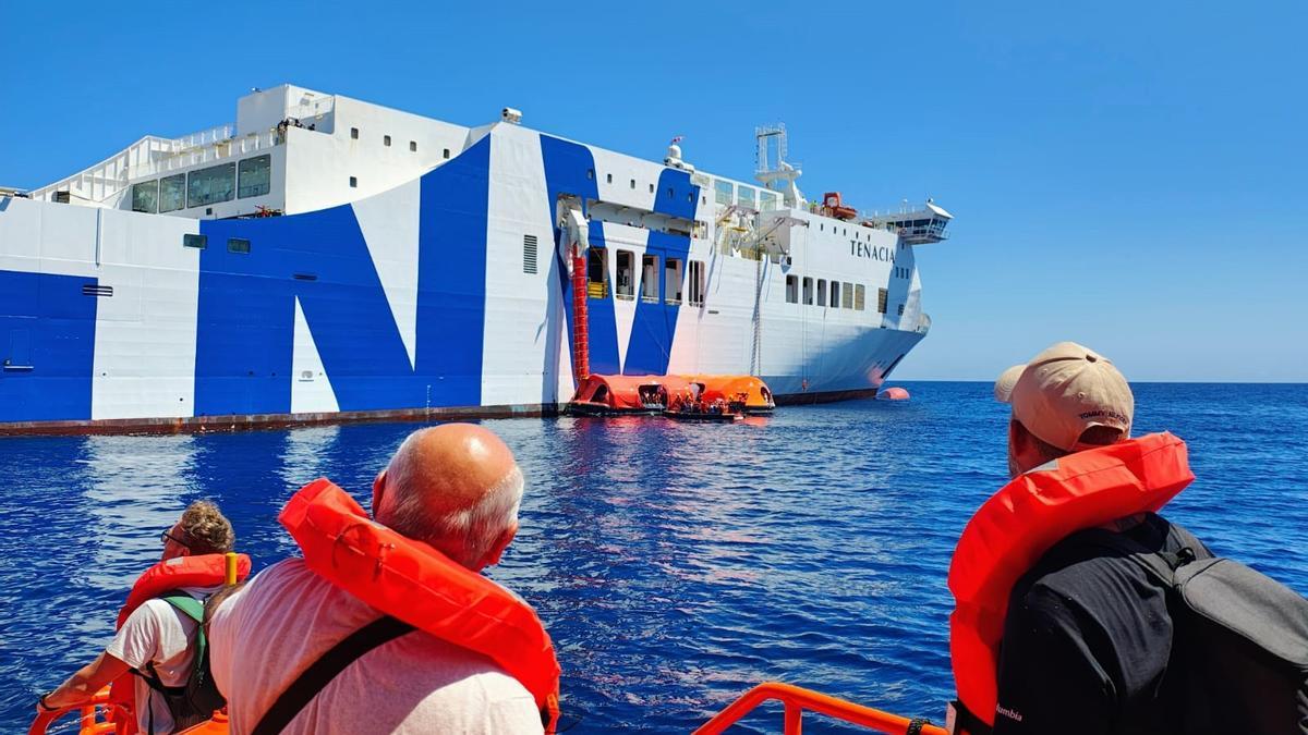 Drei Passagiere blicken von einem Rettungsboot aus auf die verunglückte Fähre Tenacia.