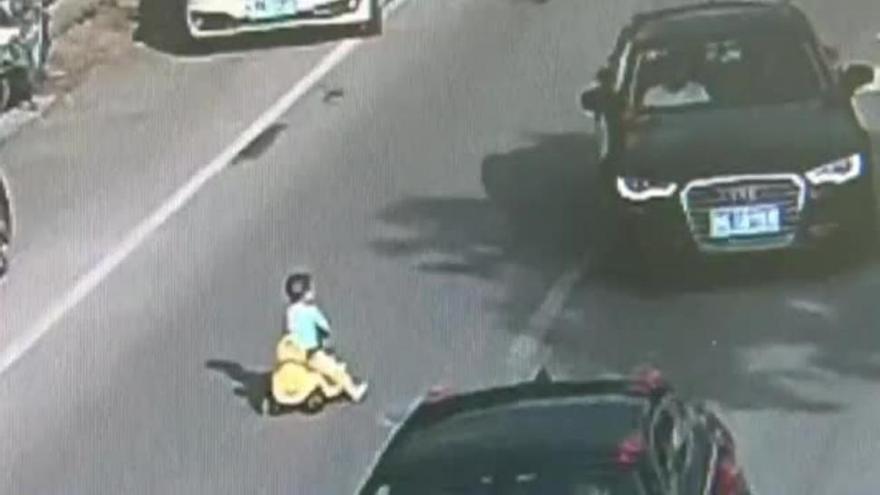 Un niño chino se mete con su cochecito de juguete en la carretera