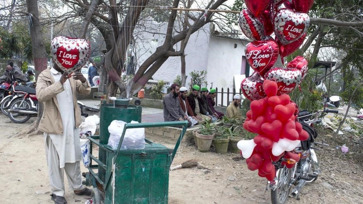 Un vendedor hincha globos de San Valentín al lado de un grupo de personas que rezan, el 14 de febrero del 2017, en Islamabad.