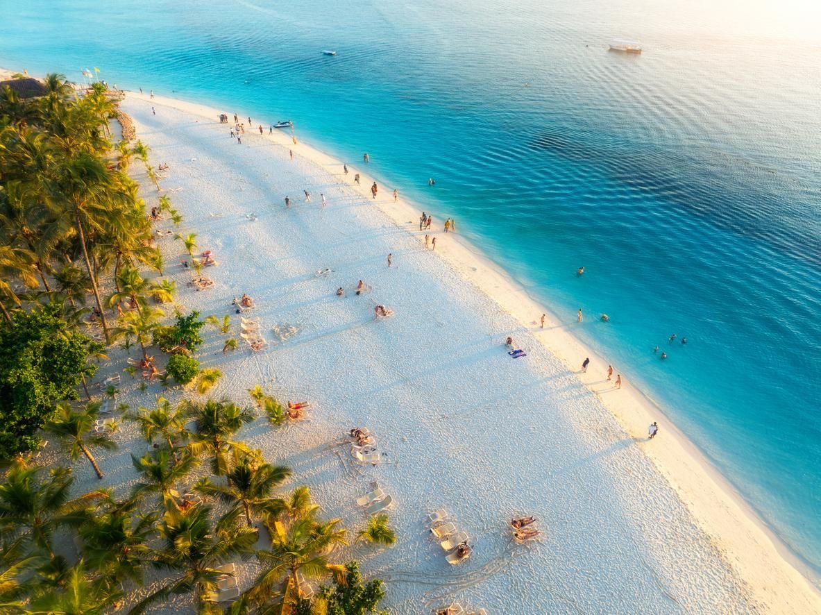 Vacaciones de verano en Kendwa, isla de Zanzíbar; paisaje tropical con palmeras, arena blanca, mar azul claro.