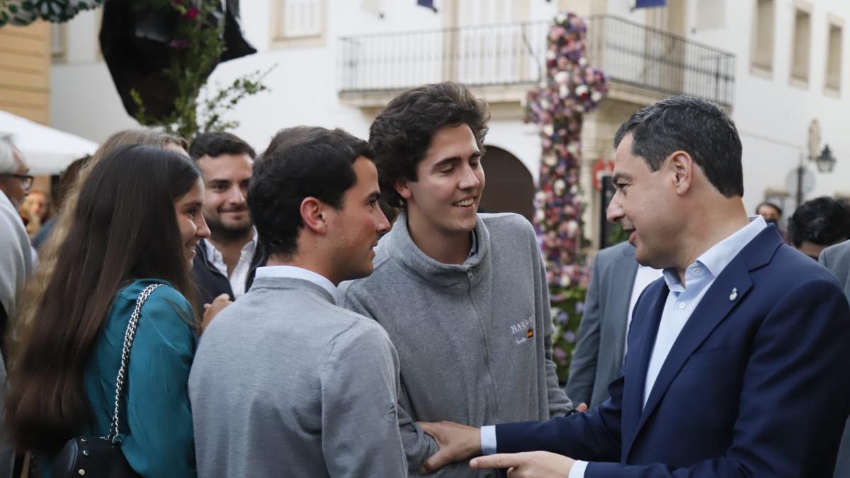 Juanma Moreno conversa con un grupo de jóvenes en una cruz de mayo.