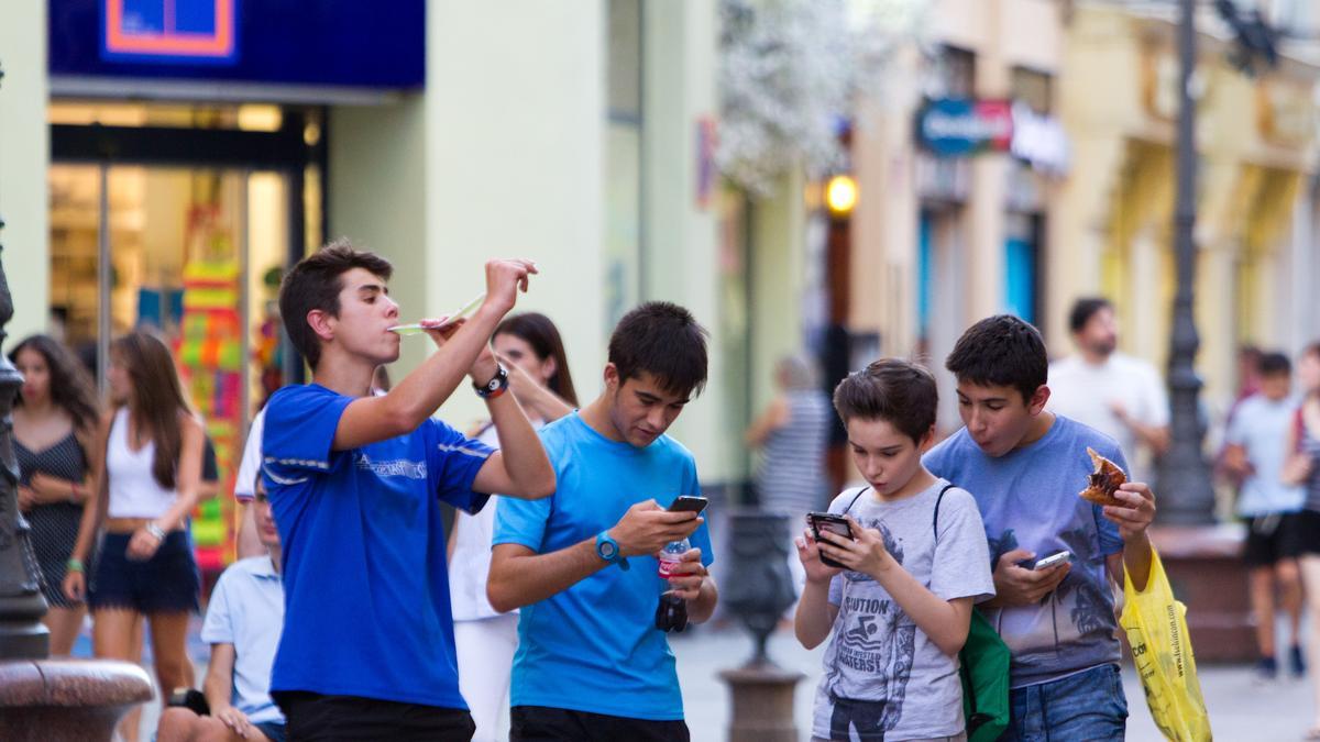 Unos jóvenes con sus móviles en la mano mientras caminan por las calles de Zaragoza.