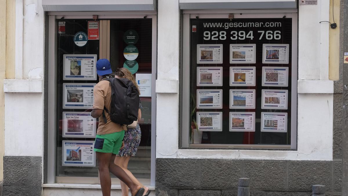 Una pareja camina por delante de una agencia inmobiliaria en Canarias.